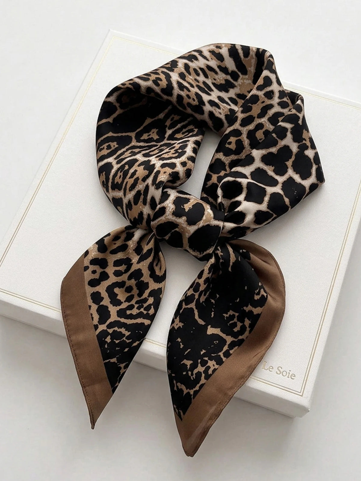 Square silk-like scarf with geometric pattern, designed by Corporación Turística, shown in a close-up image.