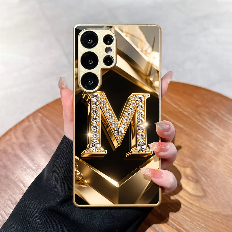 Clear diamond-letter M phone case from Corporación Turística, featuring a sparkling gold letter design on transparent material.