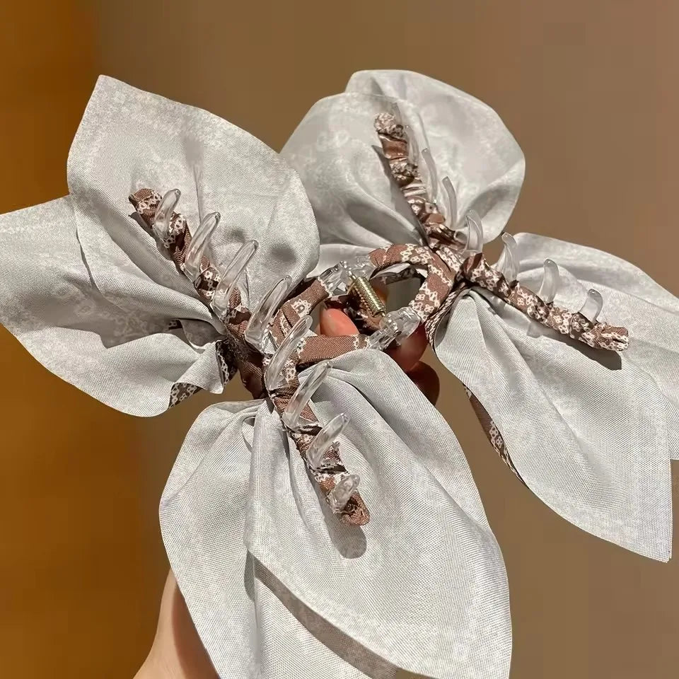 Cream-colored fabric hair clip with a floral bow design, ideal for securing hair and adding a decorative touch.