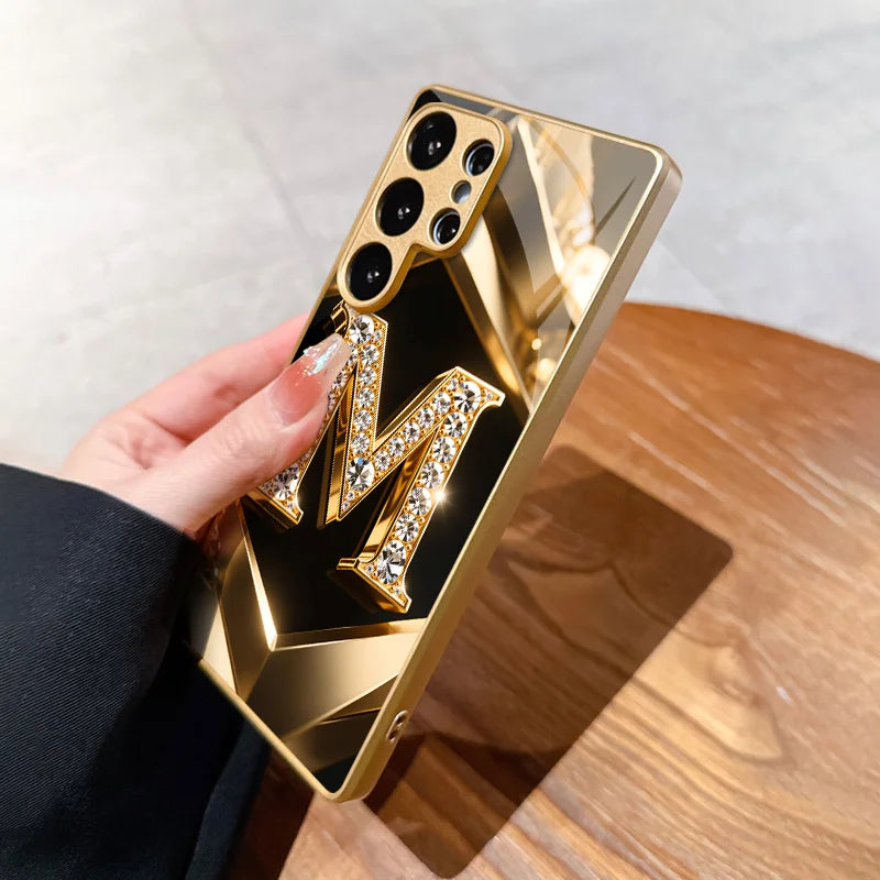 Clear glass phone case with diamond-encrusted letter M design, showcasing elegant protection for a smartphone.